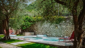 Un espace piscine entouré de murs en pierre, avec des chaises longues et un chemin.