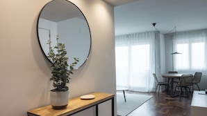 A modern room with a round mirror, a potted plant, a wooden console table, a dining area with a table and chairs, and a herringbone-patterned floor. - Charming 3-bedroom apartment in Zarautz, close to the beach (Zarauz)
