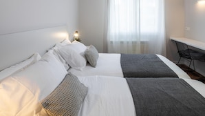 A modern hotel room with two beds, a desk, and a large window with sheer curtains. - Charming 3-bedroom apartment in Zarautz, close to the beach (Zarauz)