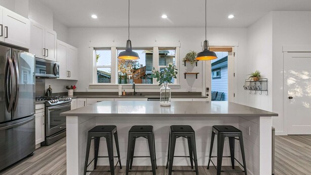 A modern kitchen with a central island, stainless steel appliances, and black bar stools.