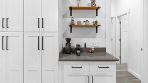 A modern kitchen with white cabinets, a dark countertop, and two wooden shelves with kitchen items.