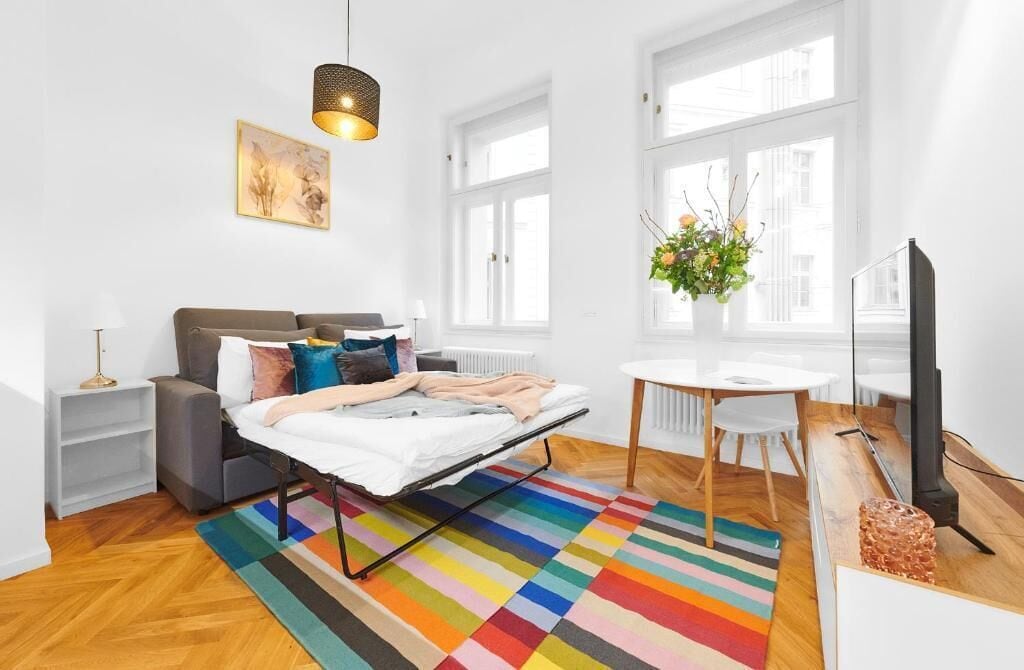 Ein moderner, gut beleuchteter Raum mit einem Bett, einem kleinen Tisch, einem Sessel und einem Fernseher.