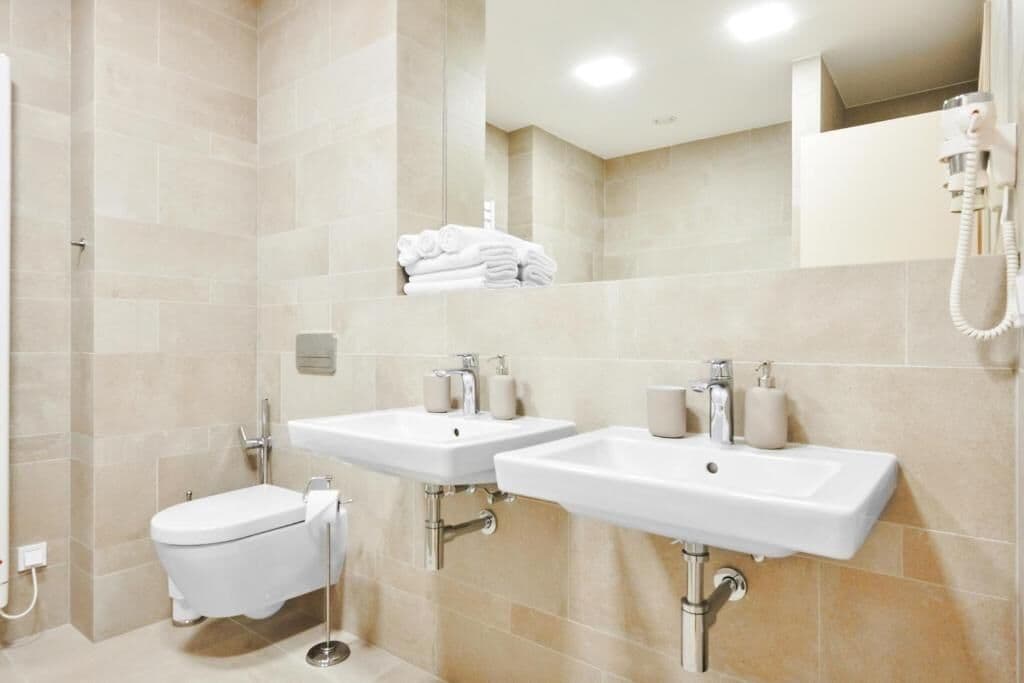 Een moderne badkamer met twee wasbakken, een toilet en een handdoekhouder.