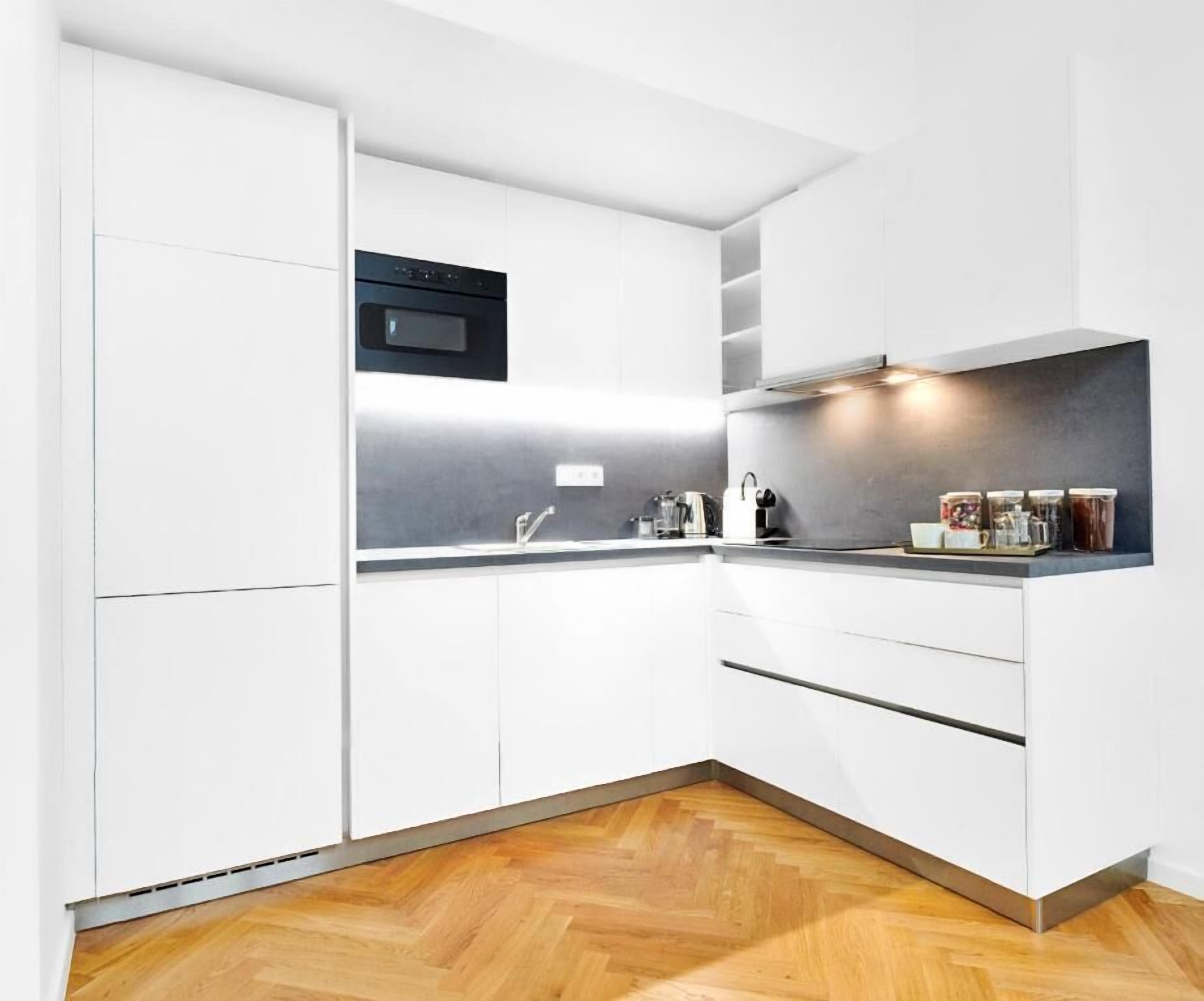 A modern kitchen with white cabinets, a black oven, and a wooden herringbone floor.