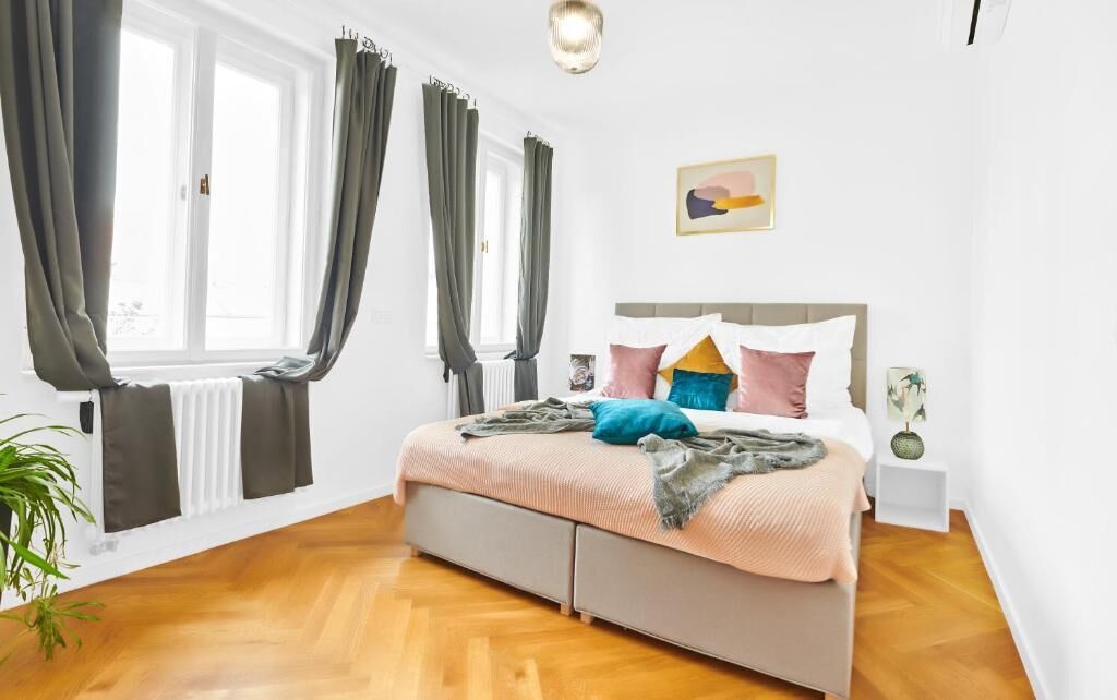 A bedroom with a bed, a nightstand, a wall-mounted artwork, and a window with curtains.