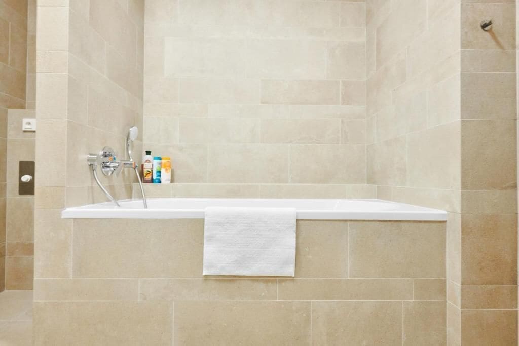 A modern bathroom with a bathtub, beige tiles, and a white towel.