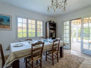 A dining room with a table set for four, a bookshelf, and a chandelier.