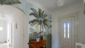 A hallway with a mural of tropical leaves, a wooden wine rack, a white door with stained glass windows, and a white chair. - Cozy Family Home in Parentis-en-Born: 3BR, WiFi, Large Garden, Near Beach & Lake (Parentis-en-Born)