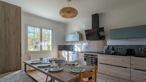 A modern kitchen with a dining table set for four, a built-in oven, and a large window providing natural light. - Cozy Family Home in Parentis-en-Born: 3BR, WiFi, Large Garden, Near Beach & Lake (Parentis-en-Born)