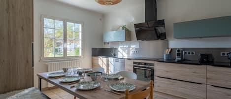 A modern kitchen with a dining table set for four, a built-in oven, and a large window providing natural light.