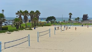 Een strandvolleybalveld met een net, palmbomen en uitzicht op de oceaan.