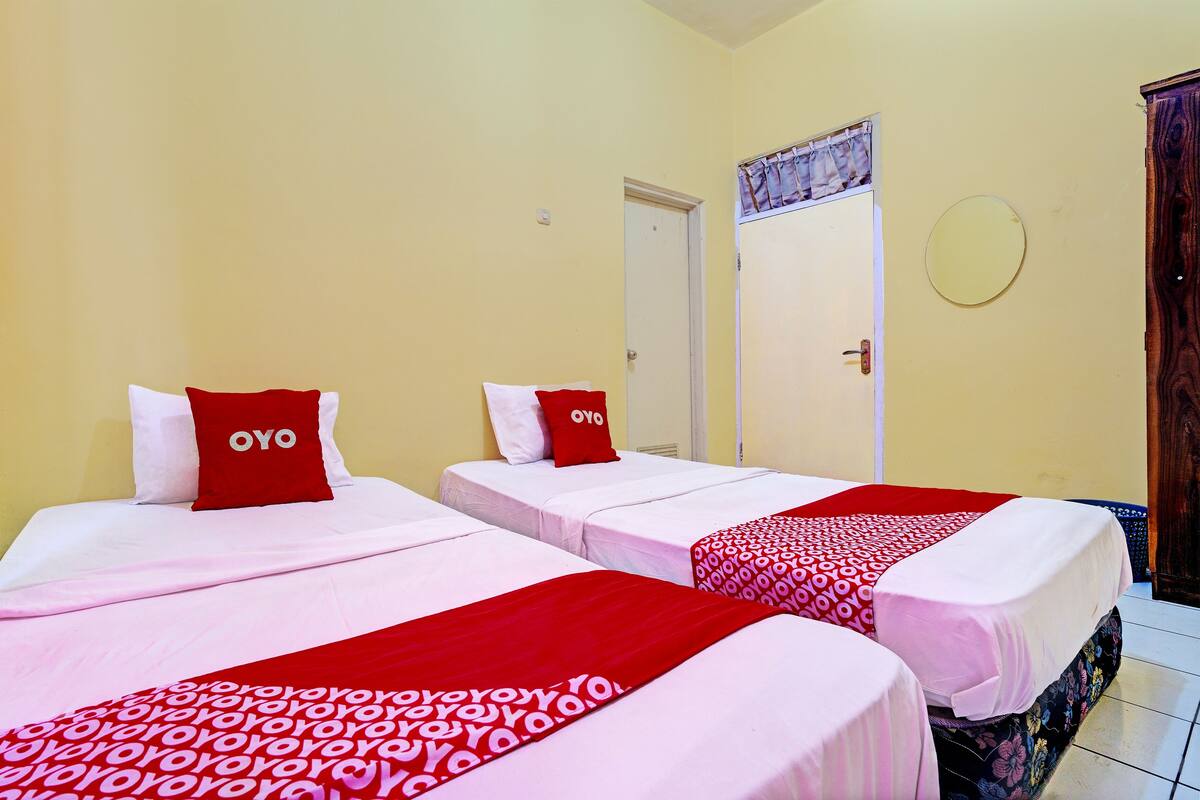 A hotel room with two beds, each with a red and white bedspread and pillows labeled "OYO".