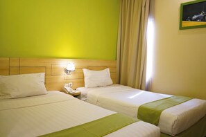 A hotel room with two beds, a wooden headboard, a bedside table with a lamp, and a telephone.