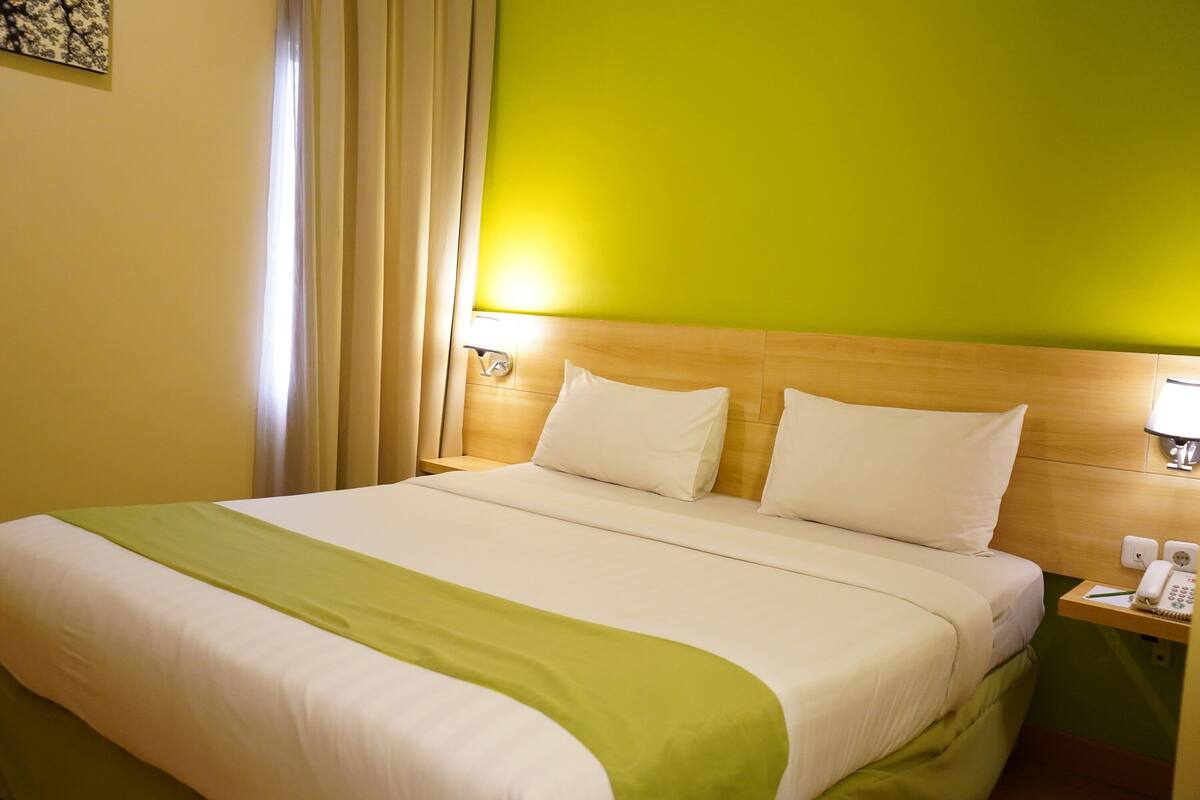 A hotel room with a large bed, a green accent wall, and a nightstand with a phone and lamp.