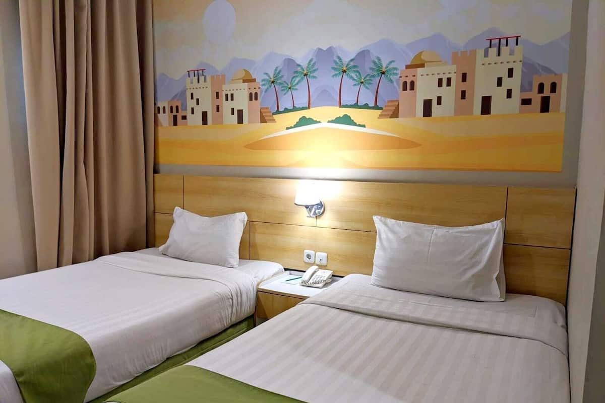A hotel room with two beds, a wooden headboard, a painting of a desert landscape, and a nightstand with a phone.