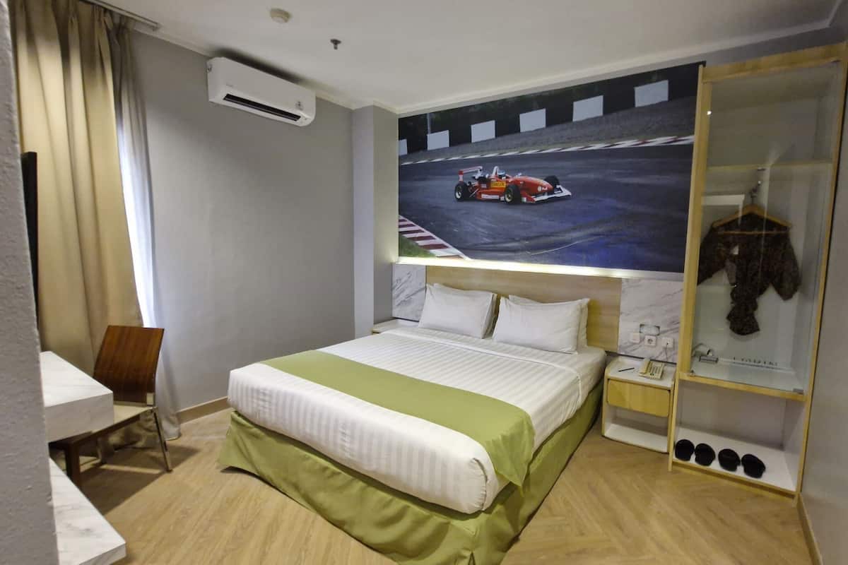 A hotel room with a bed, a desk, a chair, a wardrobe, and a racing car poster on the wall.