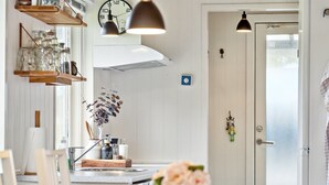 Une cuisine moderne avec des étagères en bois, une horloge, des luminaires suspendus et un vase rempli de fleurs.