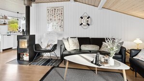 Un salon moderne avec une cheminée, un canapé en cuir noir, une table basse blanche et une pancarte « Bienvenue à bord » accrochée au mur.
