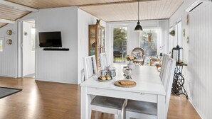 Un grand espace dédié à la salle à manger, avec une table blanche, des chaises et un téléviseur fixé au mur.