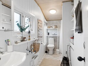 A modern bathroom with a white sink, mirror, and toilet. There are shelves with toiletries and a plant.