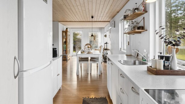 Une cuisine moderne avec des meubles blancs, un plafond en bois et une grande fenêtre offrant une vue sur l’extérieur.