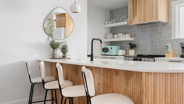 A modern kitchen with a wooden island, bar stools, pendant lights, and a large mirror. - Occasionally Luxe | Girls Trip Dream Home (Charleston)