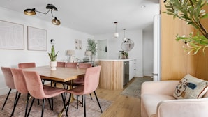 A modern kitchen with a wooden island, a dining area with pink chairs, and a living area with a sofa and a plant. - Occasionally Luxe | Girls Trip Dream Home (Charleston)