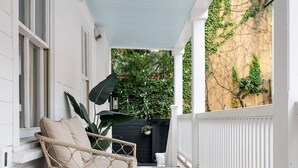 A covered porch with white railings, a wicker chair with cushions, and a white ottoman. - Occasionally Luxe | Girls Trip Dream Home (Charleston)
