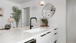 A modern kitchen with a white countertop, a sink, a black faucet, a round mirror, and a hanging pendant light. - Occasionally Luxe | Girls Trip Dream Home (Charleston)