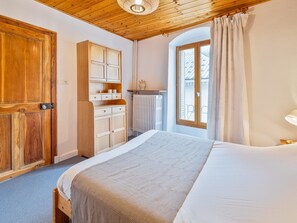 A bedroom with a wooden ceiling, a large bed, a wardrobe, and a window with curtains.