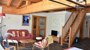 Un salón acogedor con techo de madera, un sofá rojo, un televisor y una escalera.