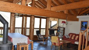 Un interior rústico de madera con suelo de piedra, una mesa con mantel blanco, una mecedora, un sofá y una estantería.