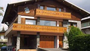 Een houten huis met twee verdiepingen, voorzien van een balkon op de eerste etage en een garage op de begane grond.