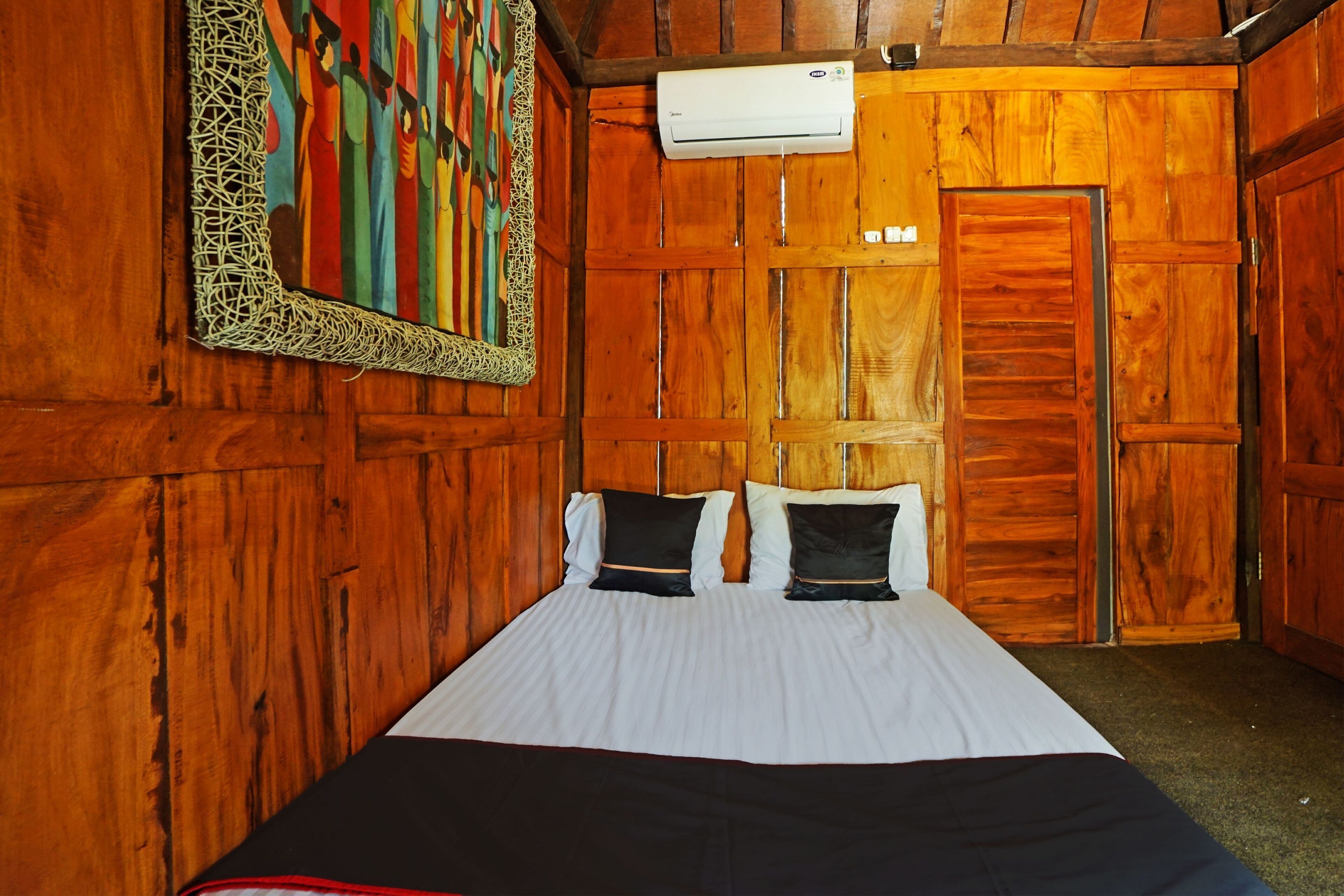 Una habitación de madera con una cama, aire acondicionado instalado en la pared y una puerta.