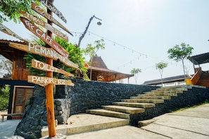 A stone staircase leading up to a building with a traditional roof, surrounded by a stone wall and a wooden signpost with various directions. - Capital O 93238 Lembah Mbalong Resort (Malang)