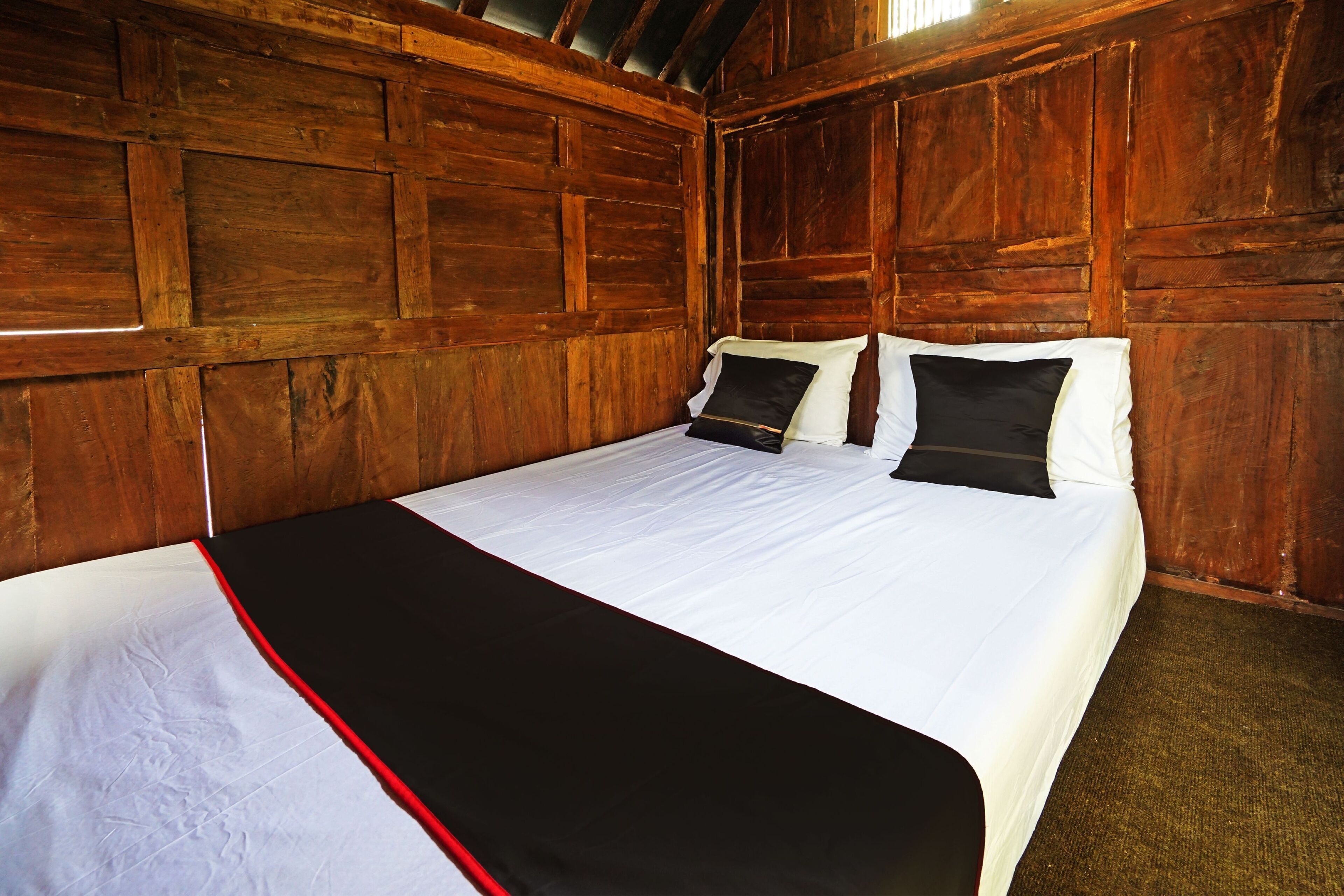 A wooden-paneled room with a bed, white bedding, and a black and red bedspread.