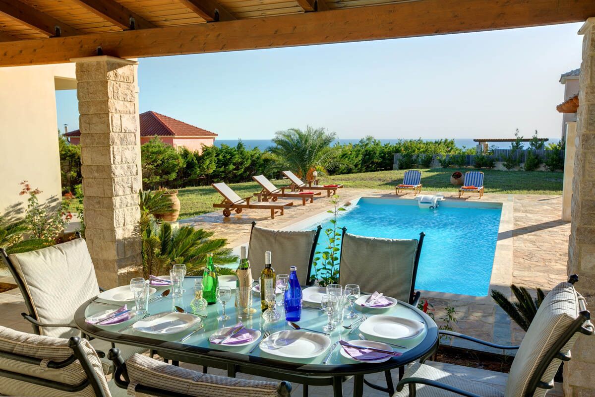 Un espace extérieur aménagé pour les repas, avec une piscine, des chaises longues et une vue sur l’océan.