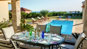 Ein Essbereich im Freien mit Pool, Liegestühlen und Blick aufs Meer.