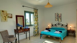 Ein Schlafzimmer mit Bett, Nachttischen, einem Sessel, einem Schreibtisch und einem fenster mit Vorhängen.