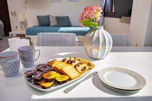 A breakfast setting with a plate of bread, butter, and jam, a vase with flowers, and a bed in the background.