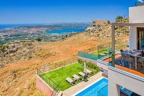 A modern villa with a rooftop pool, a terrace with lounge chairs, and a scenic view of the coastline.