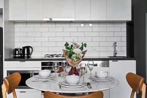 A modern kitchen with white cabinetry, a round dining table set with white plates, bowls, and glasses, and a centerpiece of flowers. - A Cozy & Chic 2BR Apt, City Views in Southbank (Southbank)