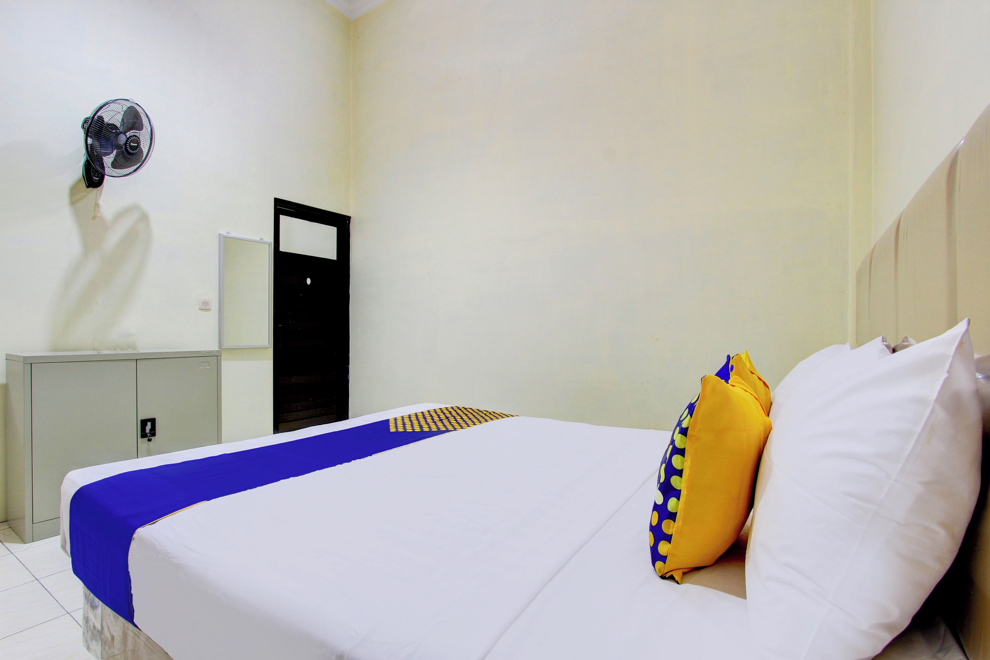 A hotel room with a bed, a wardrobe, a mirror, and a wall-mounted fan.