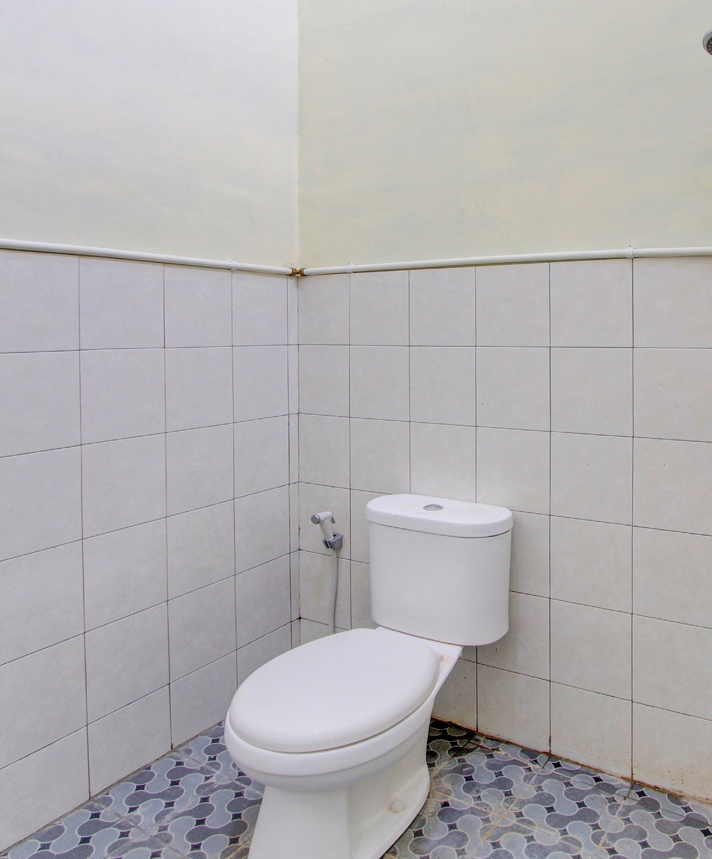 Een kleine betegelde badkamer met een wit toilet, een betegelde vloer en een witte muur.