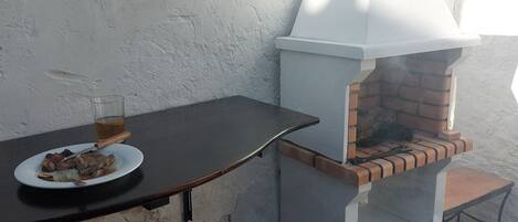 Un espacio de comedor al aire libre rústico, con un horno de ladrillo, una mesa y taburetes azules.