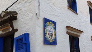 Edifici amb façana blanca, persianes blaves i un rètol blau i daurat que diu "CASA DE M. BAREA".