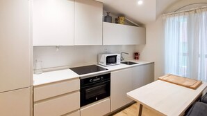 Une cuisine compacte avec des meubles blancs, un four à micro-ondes, un évier et une petite table.