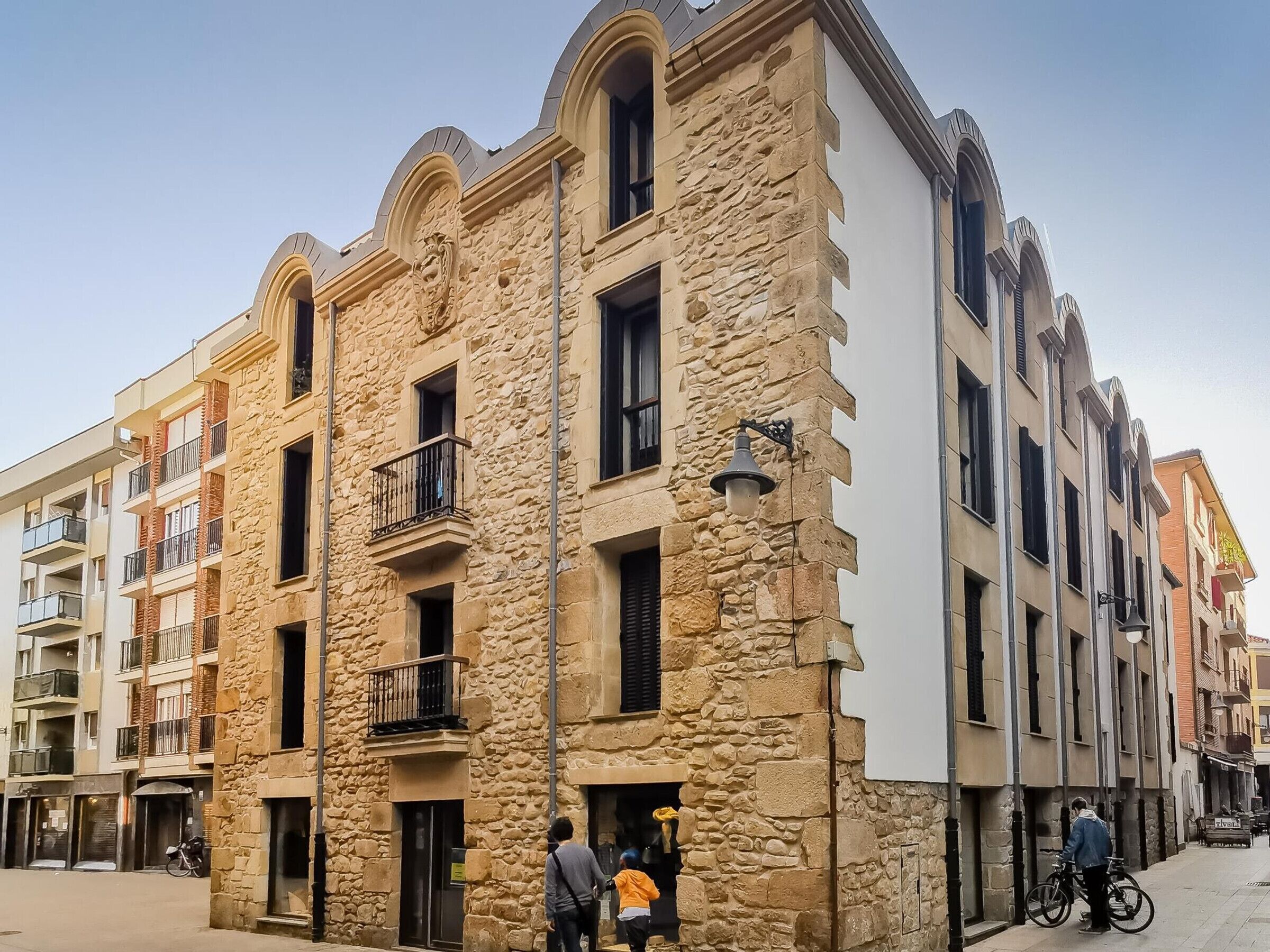 A multi-story building with stone facade, balconies, and a street view.
