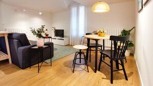 Un salon moderne avec un canapé, une table à manger et des chaises, un téléviseur et un luminaire suspendu.