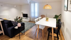 Un salon moderne comprenant un canapé, une table à manger, des chaises, un téléviseur, une plante et un luminaire suspendu.